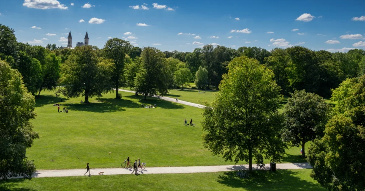 Aerial view of a sunny park with trees, pathways, and people walking and relaxing on the grass.